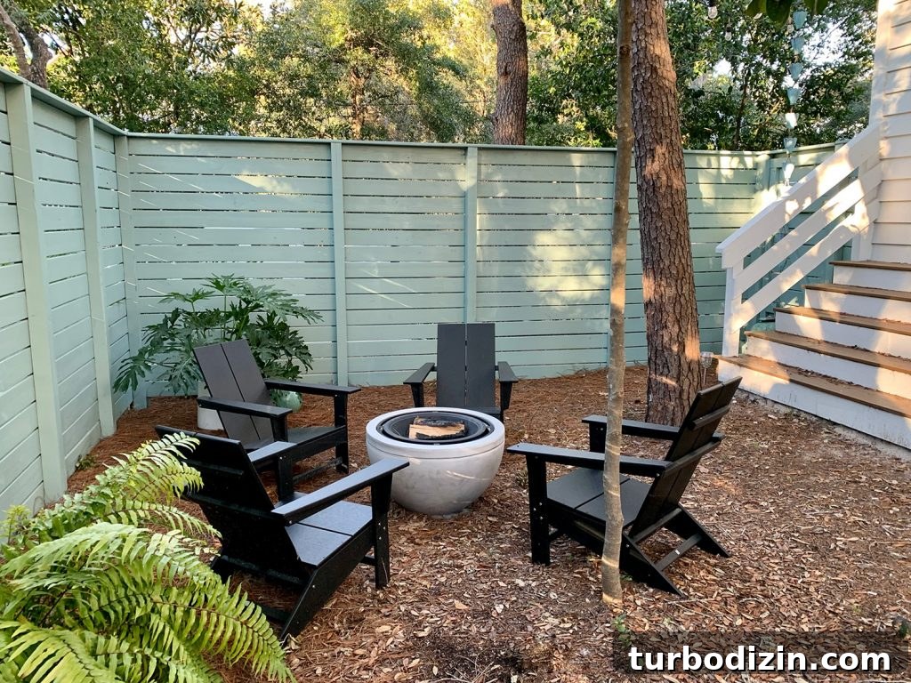 Painted fenced side yard with black Adirondack chairs around fire pit with potted plants