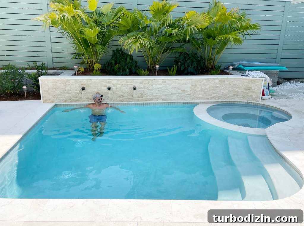 John in small freeform pool against stone accent retaining wall under palm plants